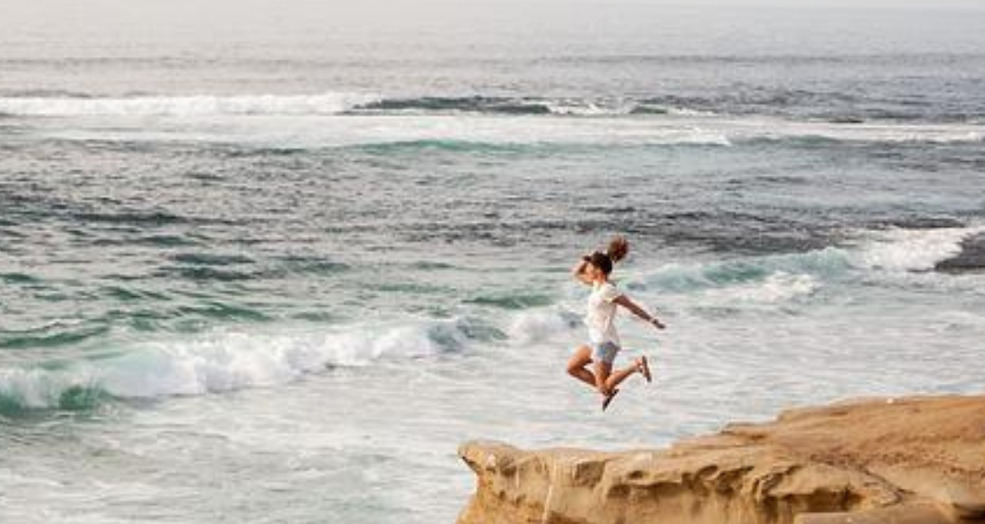 Woman jumping on cliffs in from of the ocean